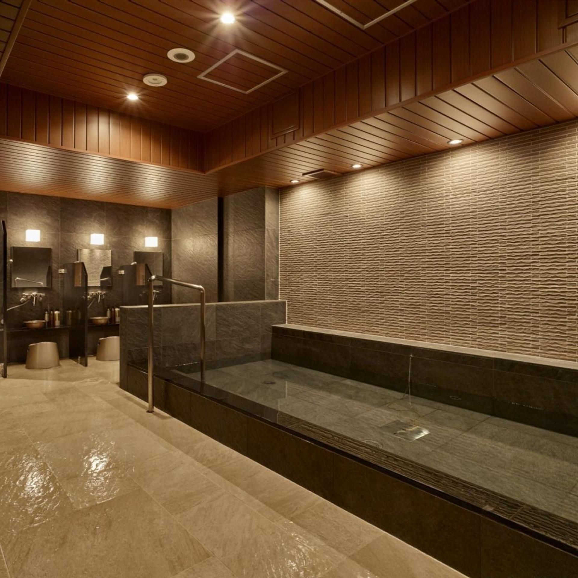 A modern bathroom with a glass-enclosed shower, dark tiled walls, and wooden ceiling panels.