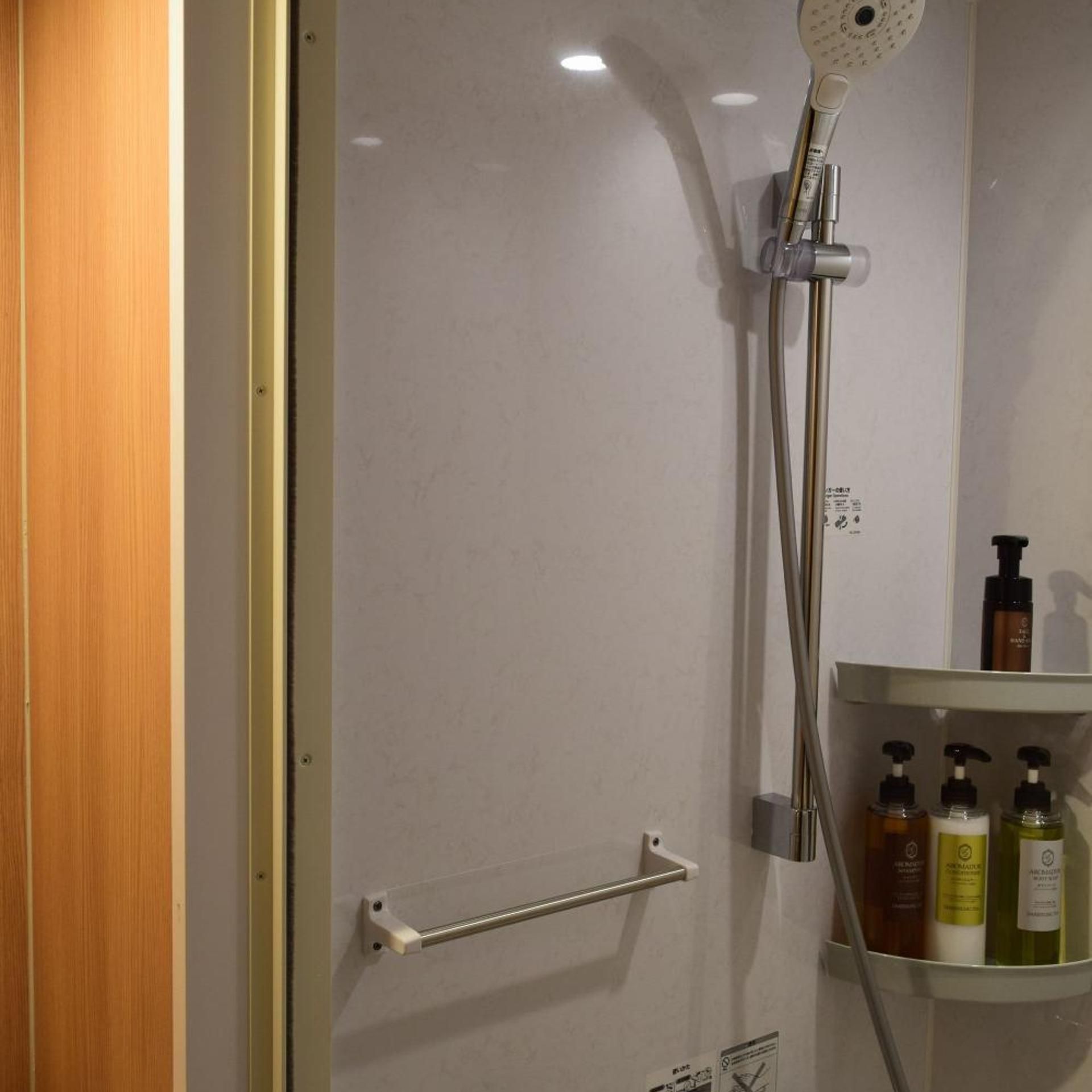 A shower with a handheld showerhead, a glass door, and a shelf with toiletries.