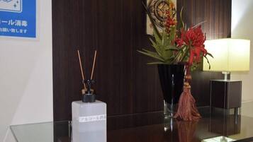Un comptoir d’accueil avec un plateau en verre, un vase décoratif contenant des fleurs rouges, une petite lampe et une enseigne fixée au mur avec du texte en japonais.