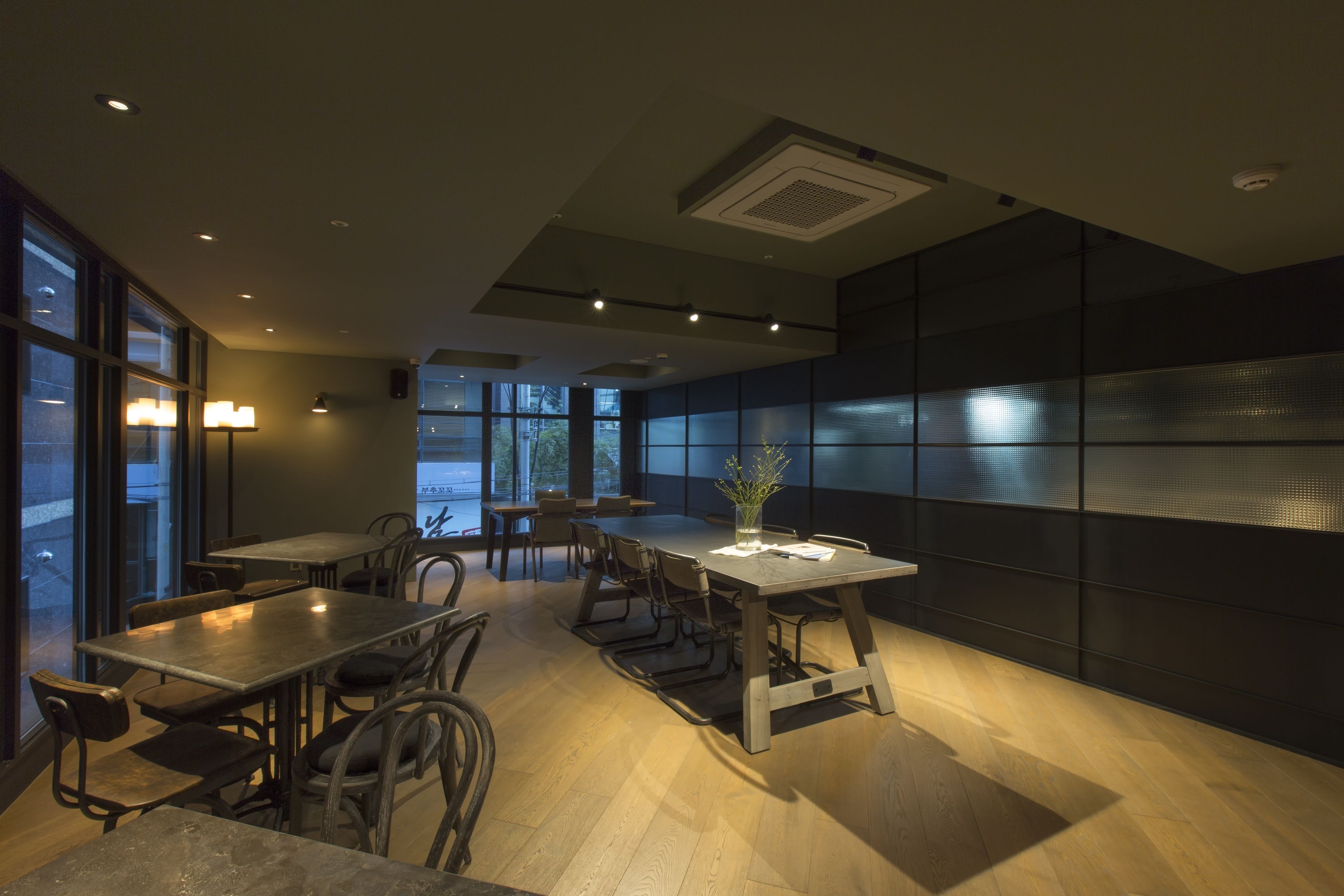 A modern dining area with multiple tables and chairs, large windows, and a decorative plant centerpiece.