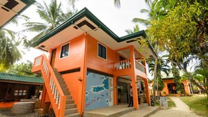 Un edificio de dos pisos con fachada naranja, una escalera que conduce a la entrada y un mural con un mapa en la pared frontal.