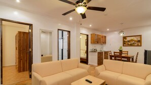 Una sala de estar con sofás color crema, un ventilador de techo y un comedor con muebles de madera.