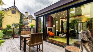 Una casa moderna con terraza, zona de comedor con mesa y sillas, y un amplio ventanal que da a un espacio interior con chimenea y mobiliario.