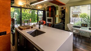 A modern kitchen with a large island, built-in appliances, and a dining area with a view of the outdoors. - Corinda Contemporary (Glebe)