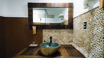 Un baño con un lavabo de piedra, tocador de madera y espejo con marco de madera.