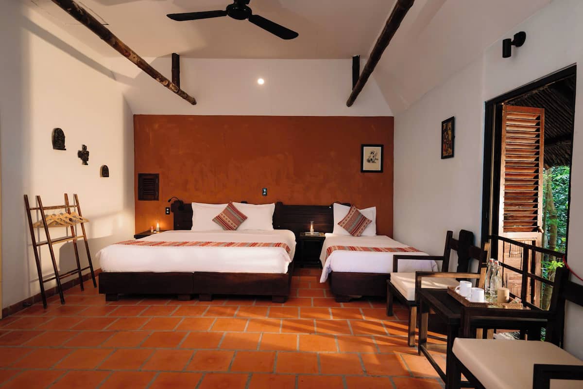 A hotel room with two beds, a dining table, and a view of the outdoors.