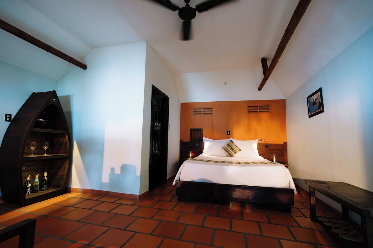 A bedroom with a bed, a wooden headboard, a nightstand, a shelf with bottles, and a ceiling fan.