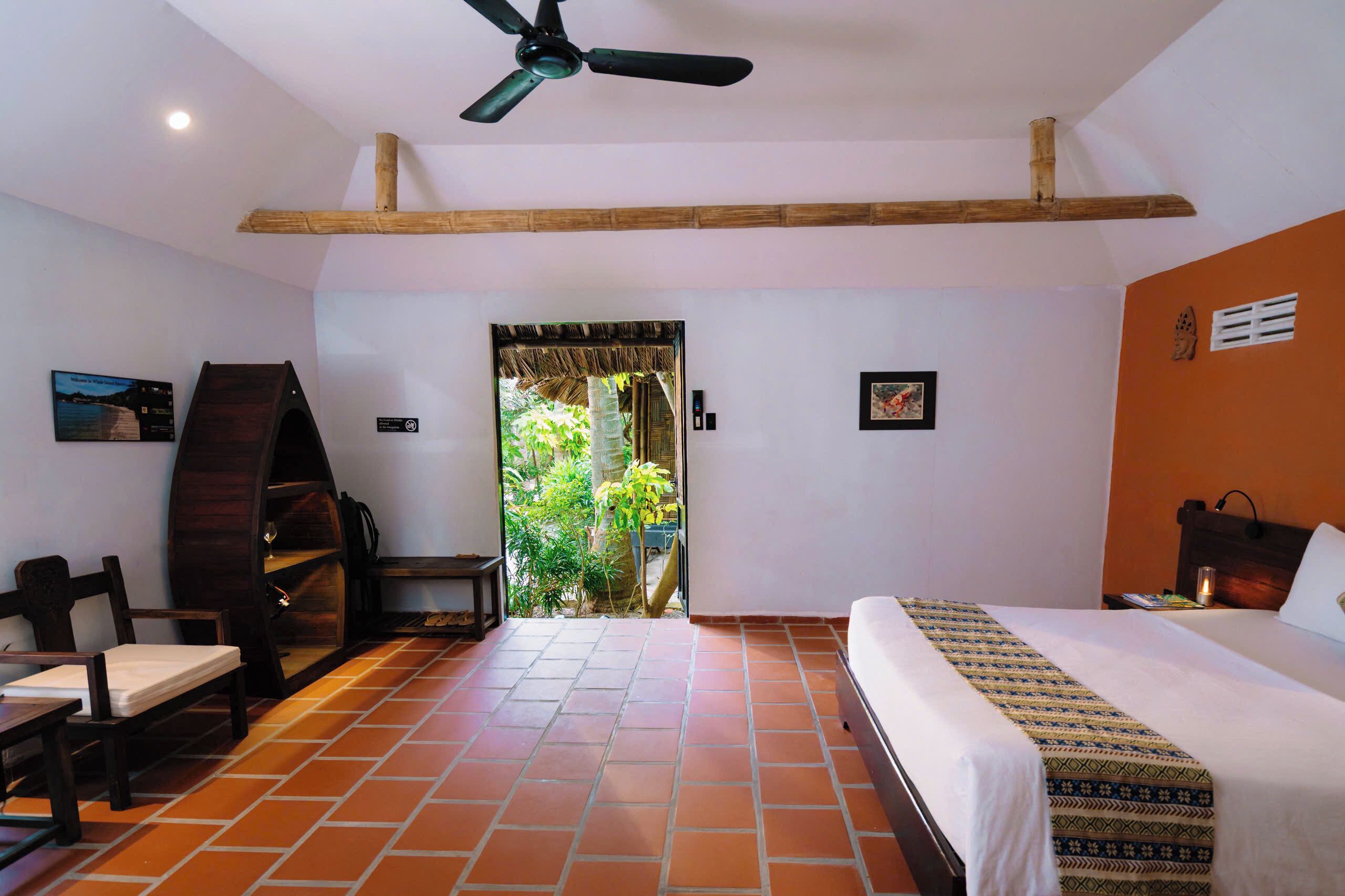 A hotel room with a bed, a desk, a chair, a ceiling fan, and a view of the outdoors.