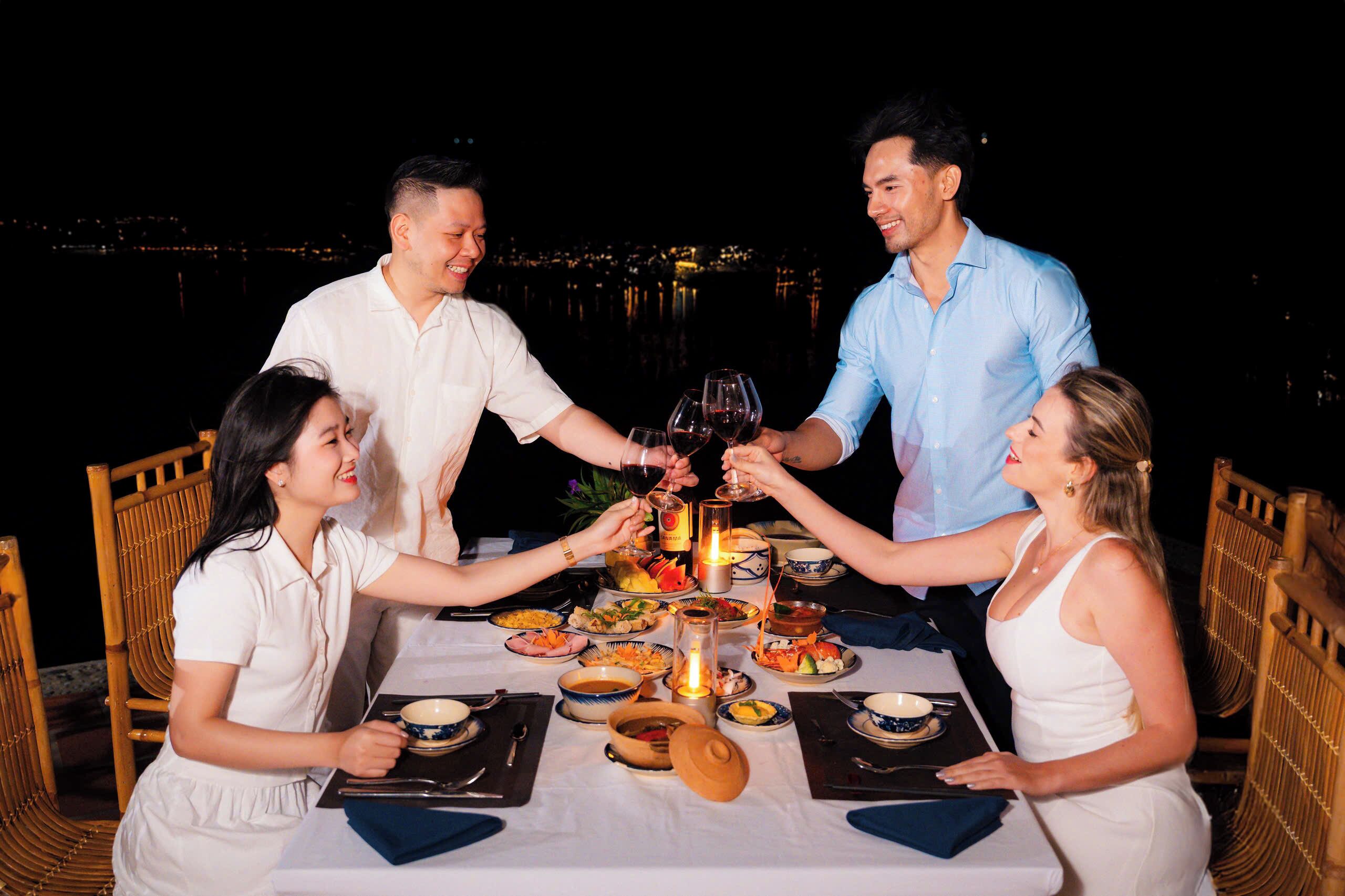 A group of people toasting at a dinner table with a view of the city at night.