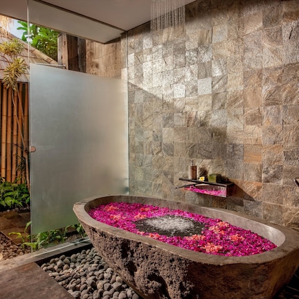 A stone bathtub filled with rose petals, surrounded by a bamboo fence and a stone wall.