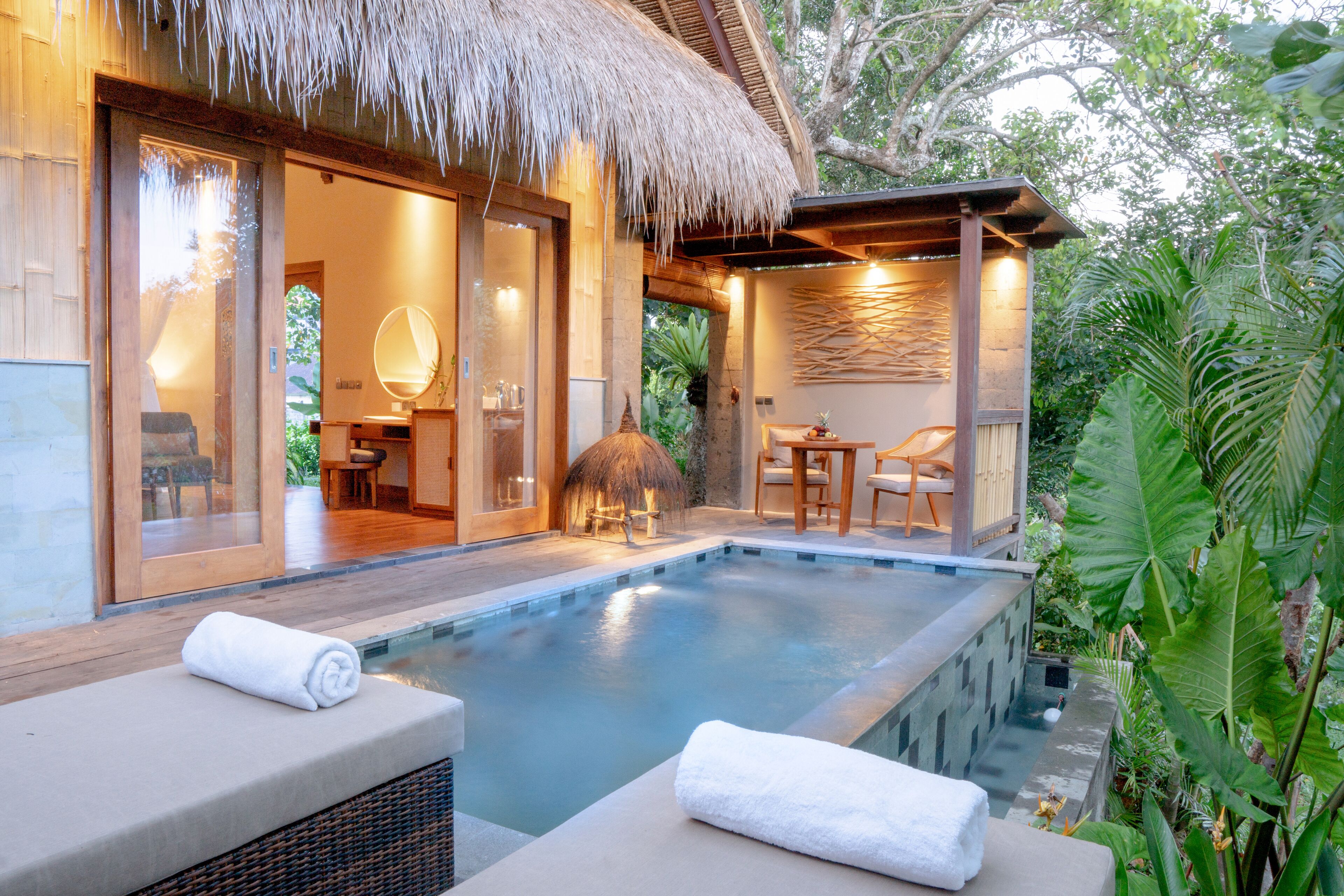 A poolside area with a thatched roof structure, wooden deck, and lounge chairs with towels.