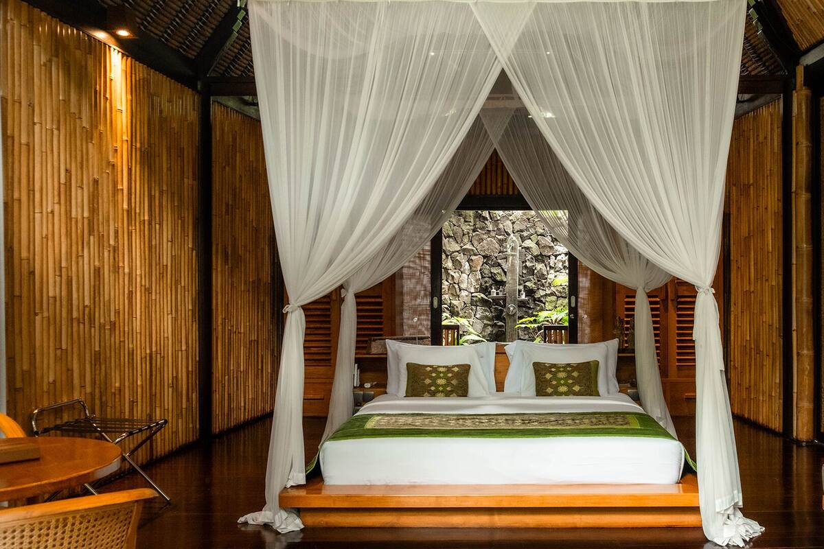 A room with a bed under a canopy, wooden walls, and a view of trees.