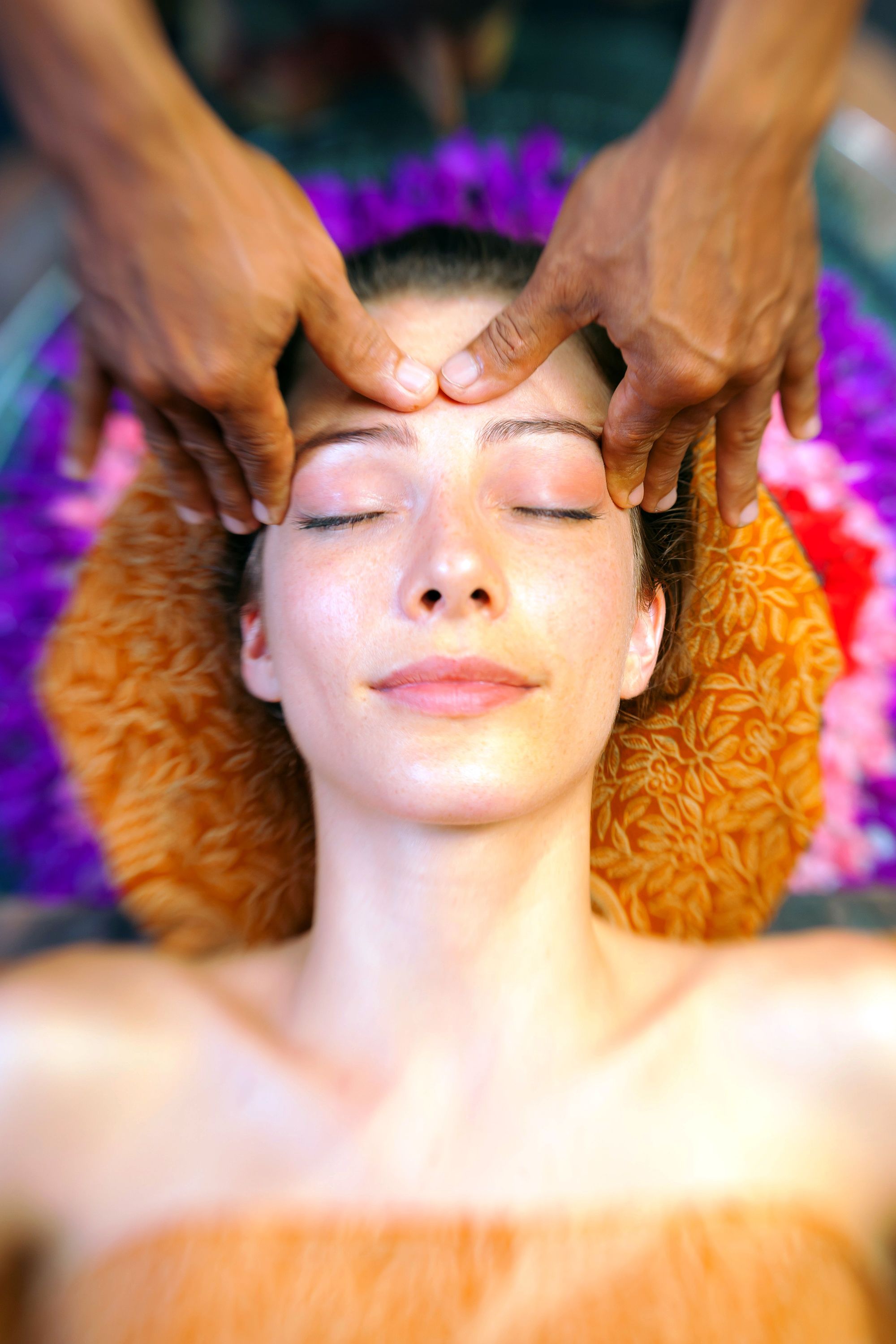 A person receiving a head massage with hands positioned on the forehead and temples.