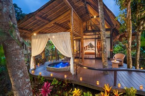 Una terraza de madera con un jacuzzi, un área de estar techada y vistas al entorno verde.