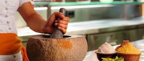 A person using a mortar and pestle, with various spices and herbs on the table.