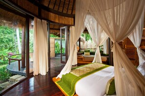 Un dormitorio espacioso con una cama grande, un balcón con terraza de madera y vistas a vegetación exuberante.