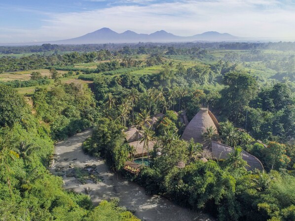 Paisaje rural con una casa tradicional de techo de paja rodeada de abundante vegetación y un río.