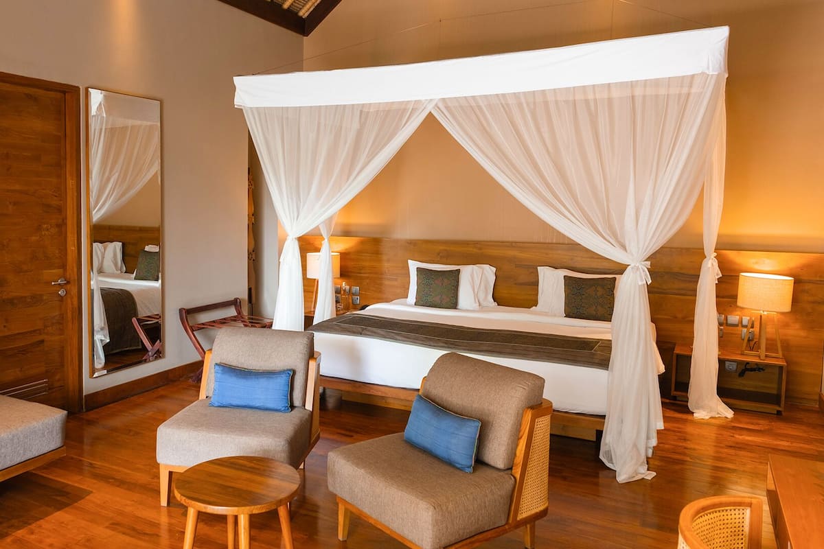 A hotel room with a large bed, two armchairs, a small table, and a mirror.