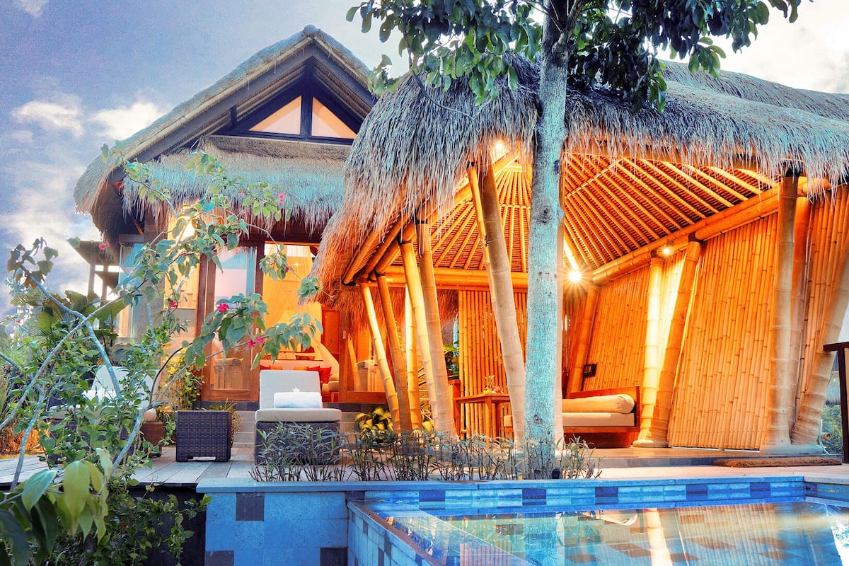 A resort with a thatched-roof structure, a pool, and lush greenery.