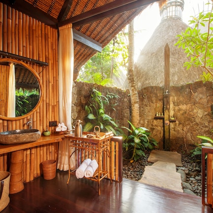 A wooden bathroom with a large mirror, a stone sink, and a small table with toiletries.