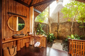 A wooden bathroom with a large mirror, a stone sink, and a small table with toiletries.