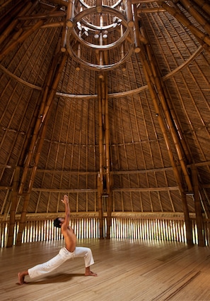 A person performing a yoga pose in a room with a high bamboo ceiling and wooden floor.