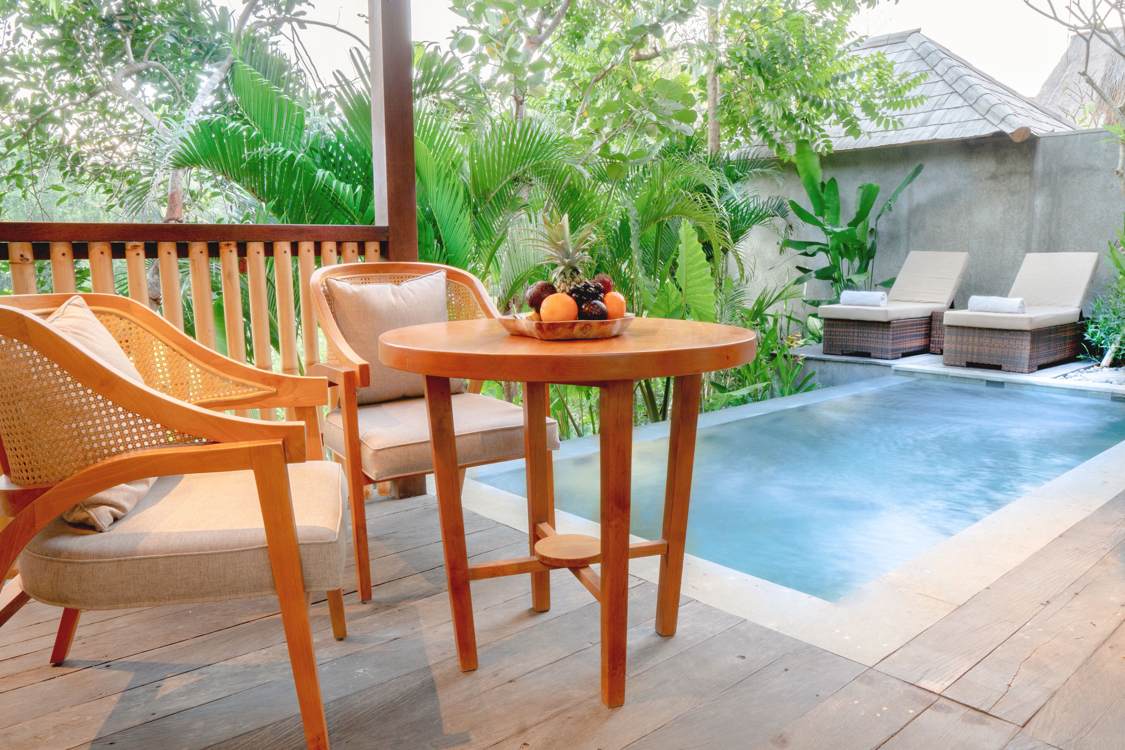 A wooden deck with a pool, lounge chairs, and a table with fruit.