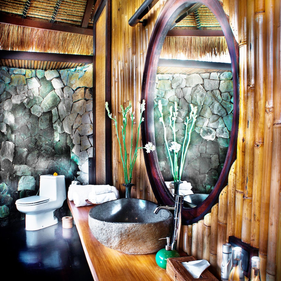 A bathroom with a stone wall, a wooden vanity, a large mirror, and a toilet.