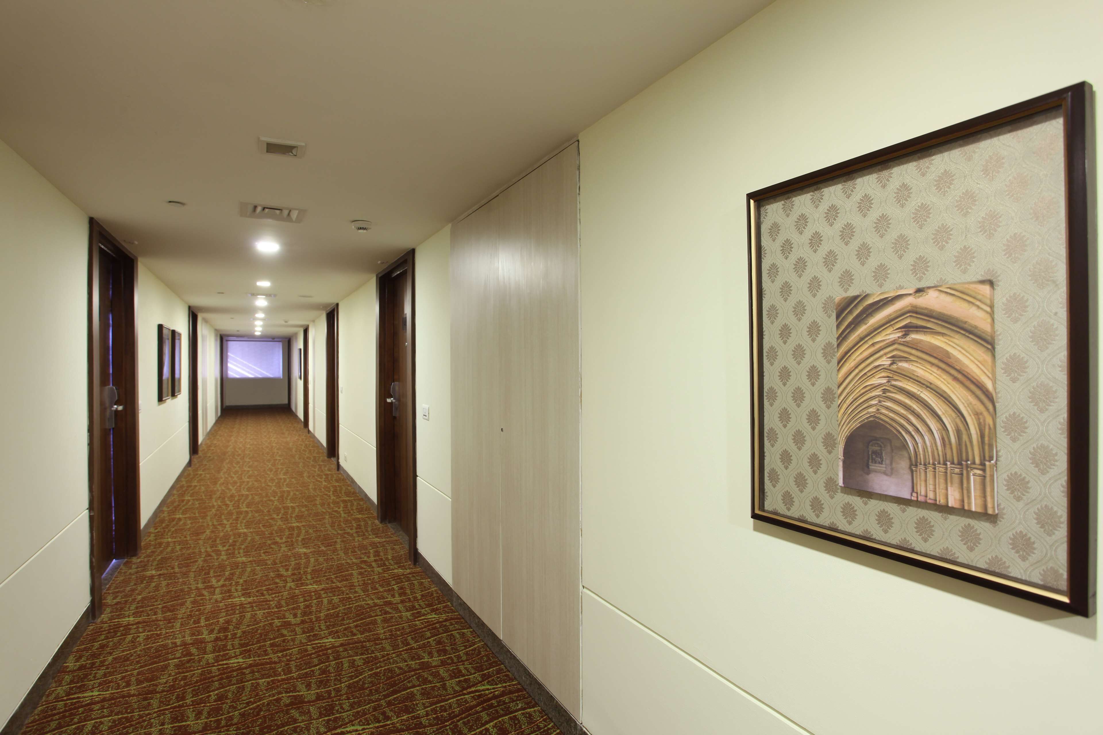Ein Hotelgang mit Teppichböden, gerahmten Kunstwerken an den Wänden und Türen zu Zimmern.