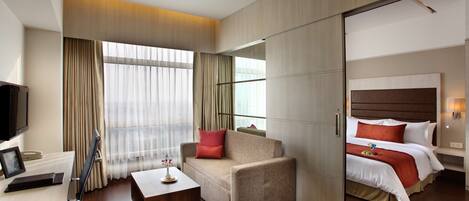 A hotel room with a sofa, a bed, a desk with a laptop, and a TV.
