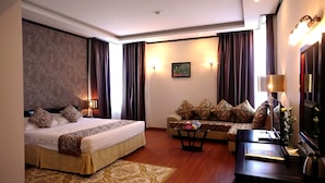 A hotel room with a bed, sofa, coffee table, and a desk with a lamp. - Golden Halong Hotel (Bai Chay)