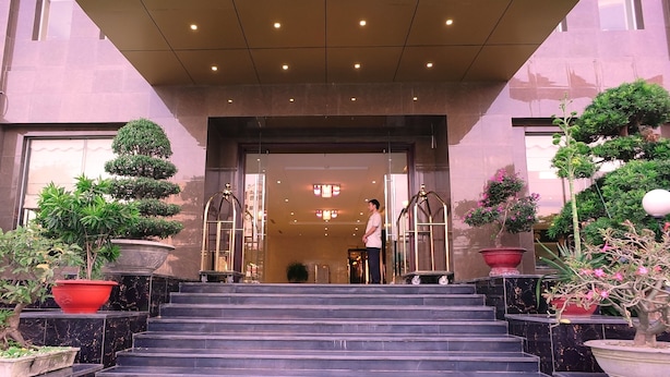 A hotel entrance with a grand staircase, a reception desk, and potted plants. - Golden Halong Hotel (Bai Chay)