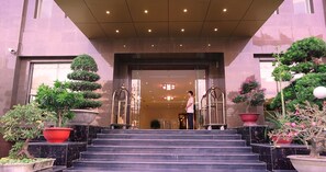 A hotel entrance with a grand staircase, a reception desk, and potted plants.