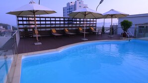 A swimming pool with lounge chairs and umbrellas, surrounded by a wooden deck and a railing. - Golden Halong Hotel (Bai Chay)