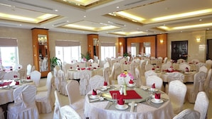 A banquet hall with round tables, white chairs, and red napkins. - Golden Halong Hotel (Bai Chay)