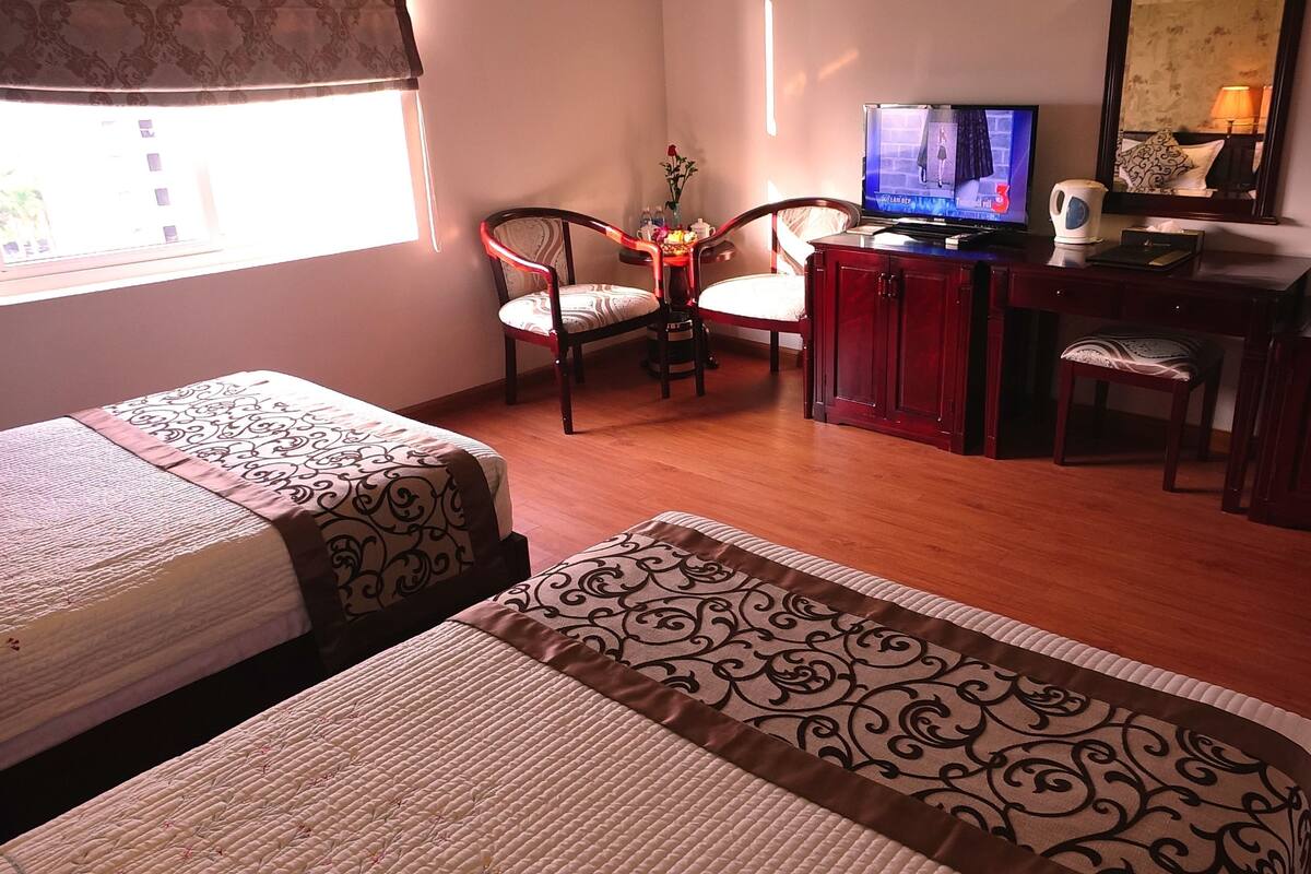 A hotel room with two beds, a TV, a desk, and a chair.