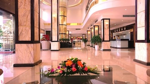 A spacious lobby with marble columns, a reception desk, and a glass coffee table with a floral arrangement. - Golden Halong Hotel (Bai Chay)