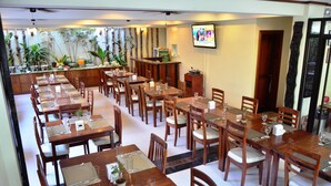 Un restaurante con varias mesas y sillas de madera, una zona de bar y un televisor en la pared.