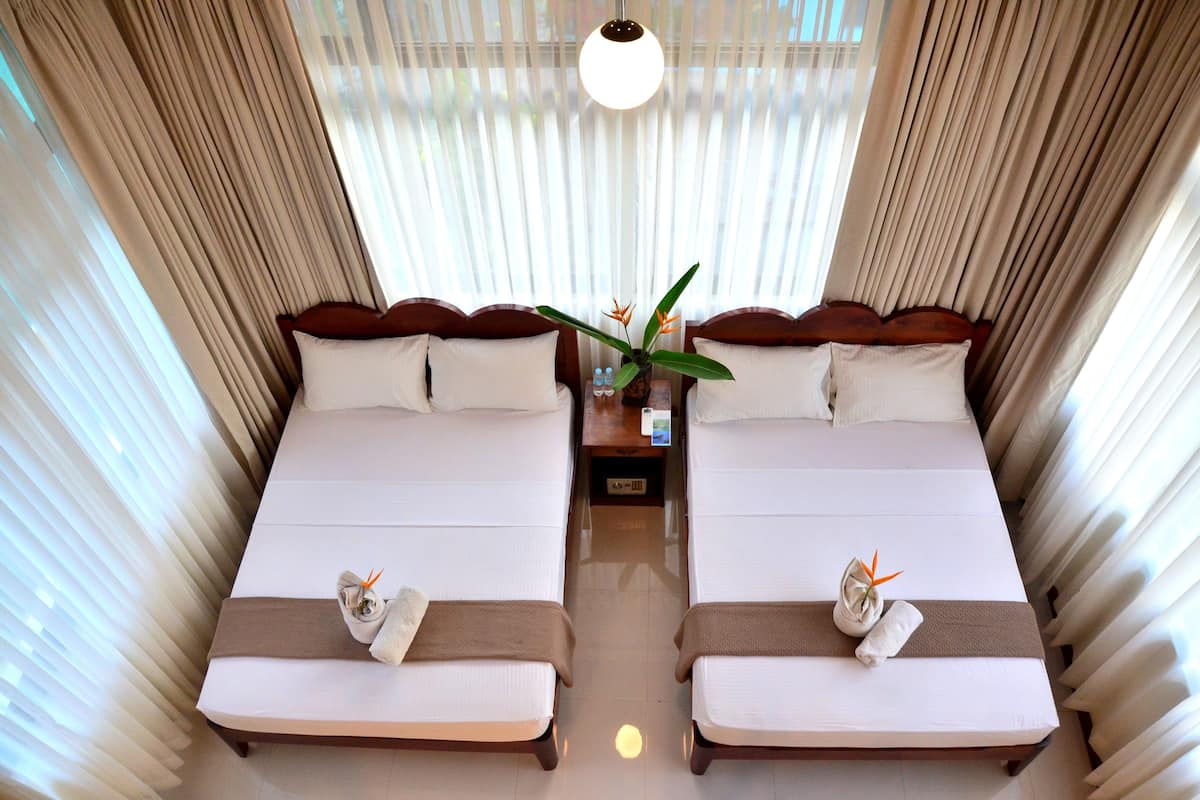 A hotel room with two beds, a nightstand, a lamp, and a window with curtains.
