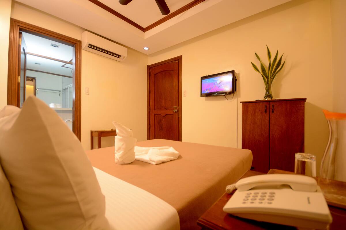 A hotel room with a bed, a TV, a telephone, and a cabinet.