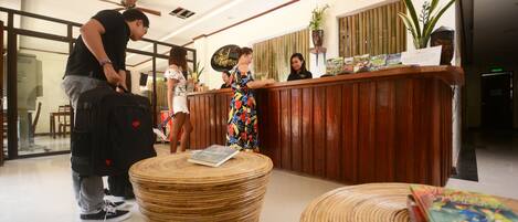 A reception area with a wooden reception desk, a receptionist, and a guest carrying luggage.