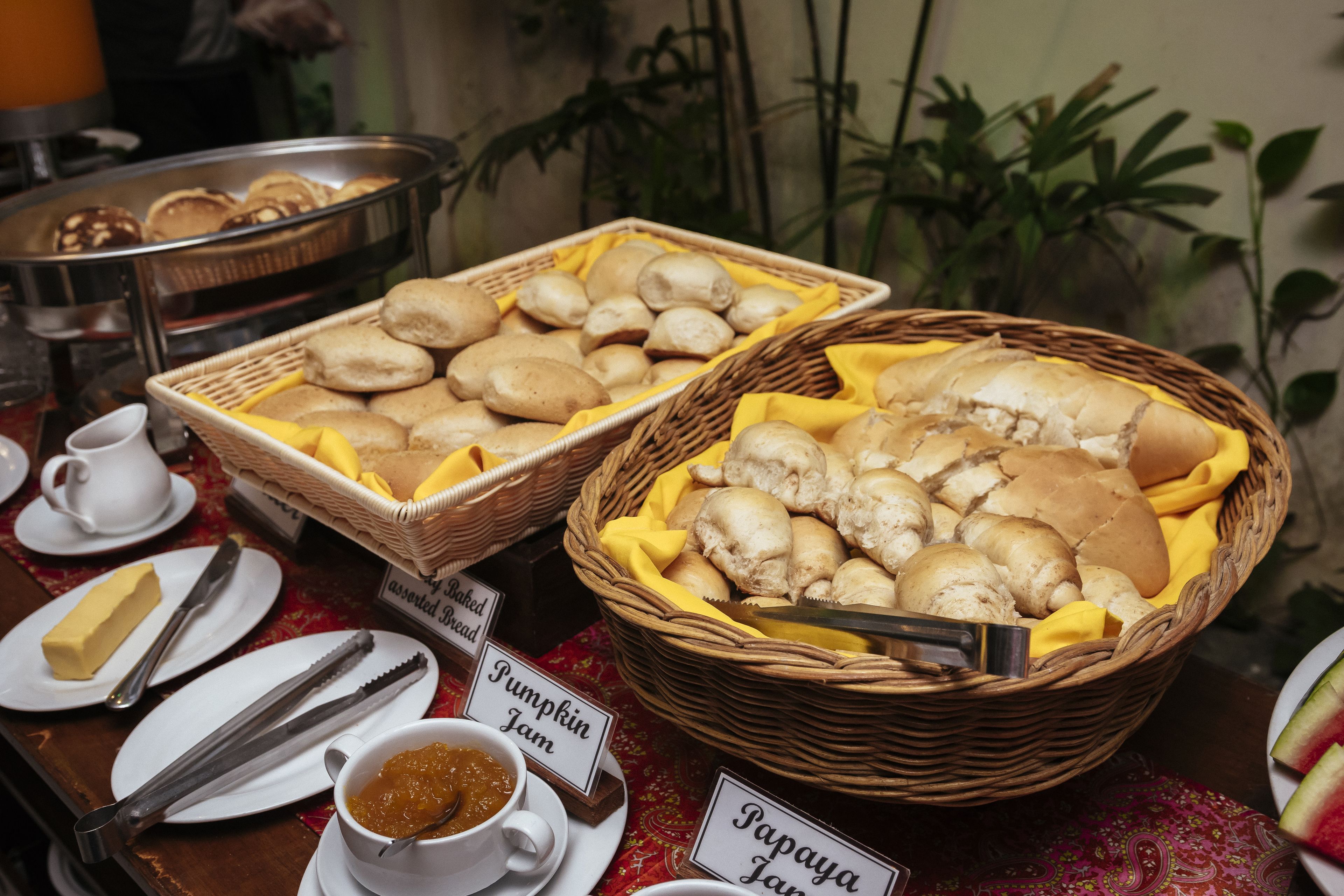 Ein Buffet mit beschrifteten Speisen, darunter Kürbiskonfitüre, Papayakonfitüre und verschiedenen Brotsorten.