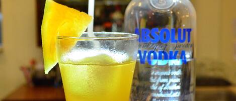 A bar setting with a tall glass of a yellow beverage, a lime wedge, and a bottle of Absolut Vodka.