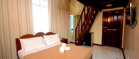 Une chambre d’hôtel avec un lit, une tête de lit en bois, des rideaux, un escalier en bois et une porte.