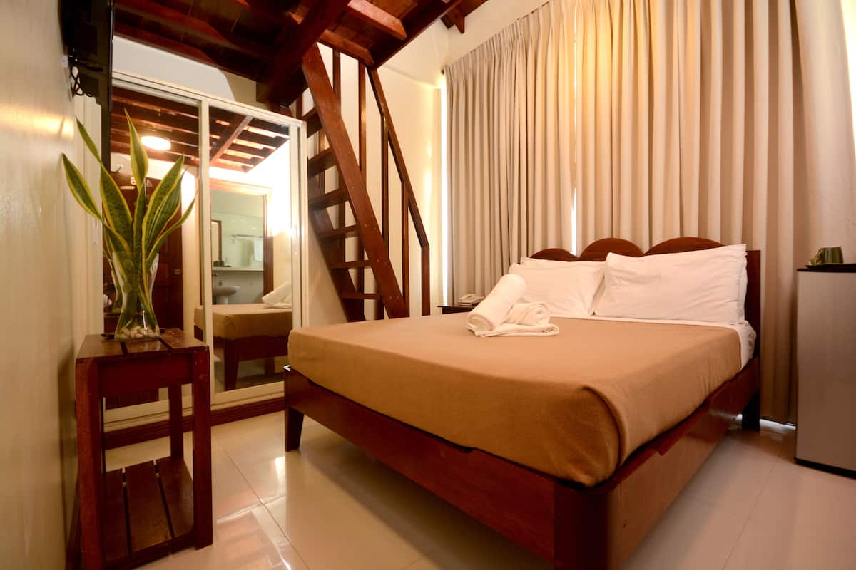 A hotel room with a wooden bed, a small table with a plant, a mirror, and a staircase.