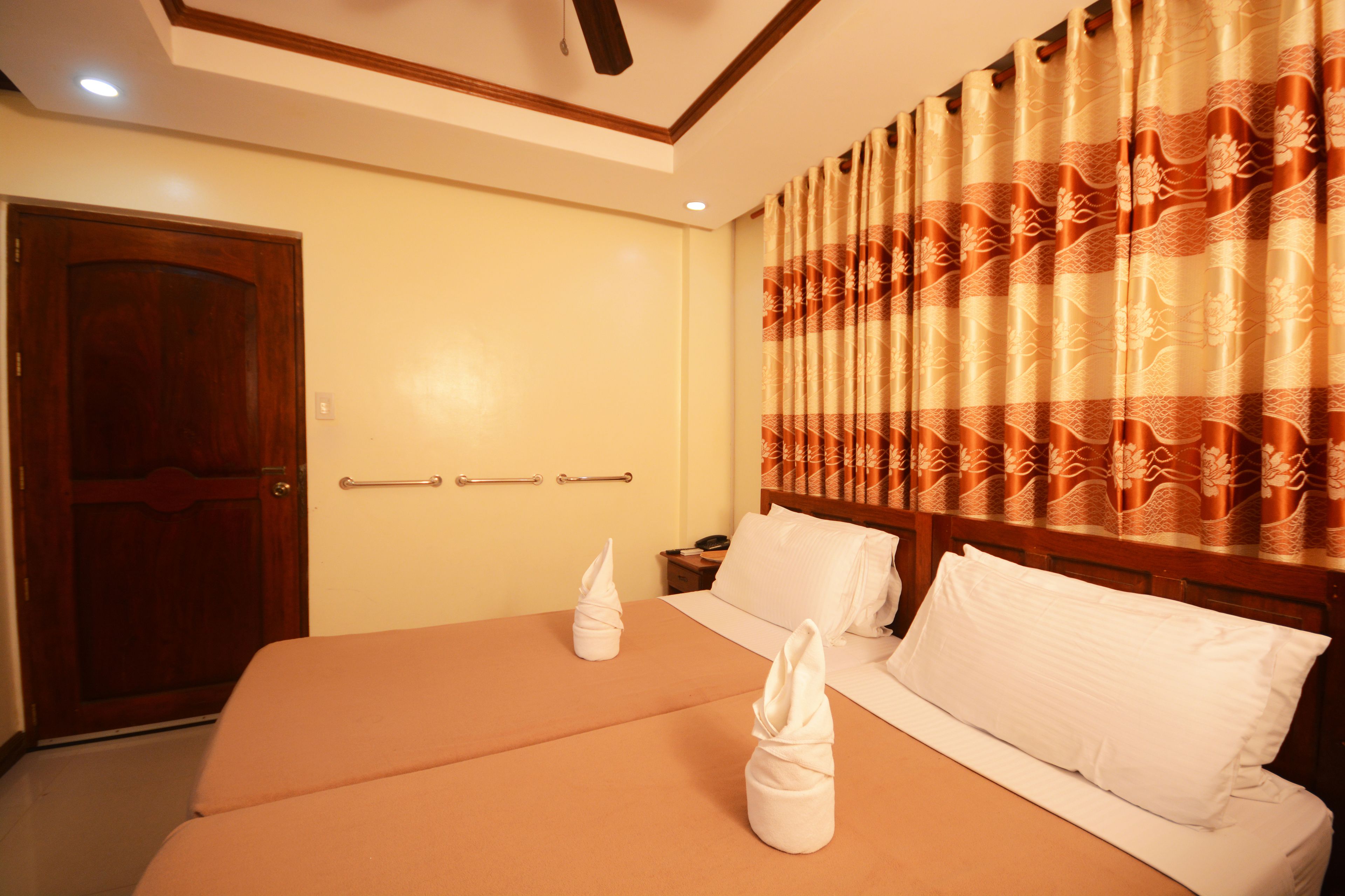 A hotel room with a double bed, two bedside tables, a wooden door, and a curtain with a floral pattern.