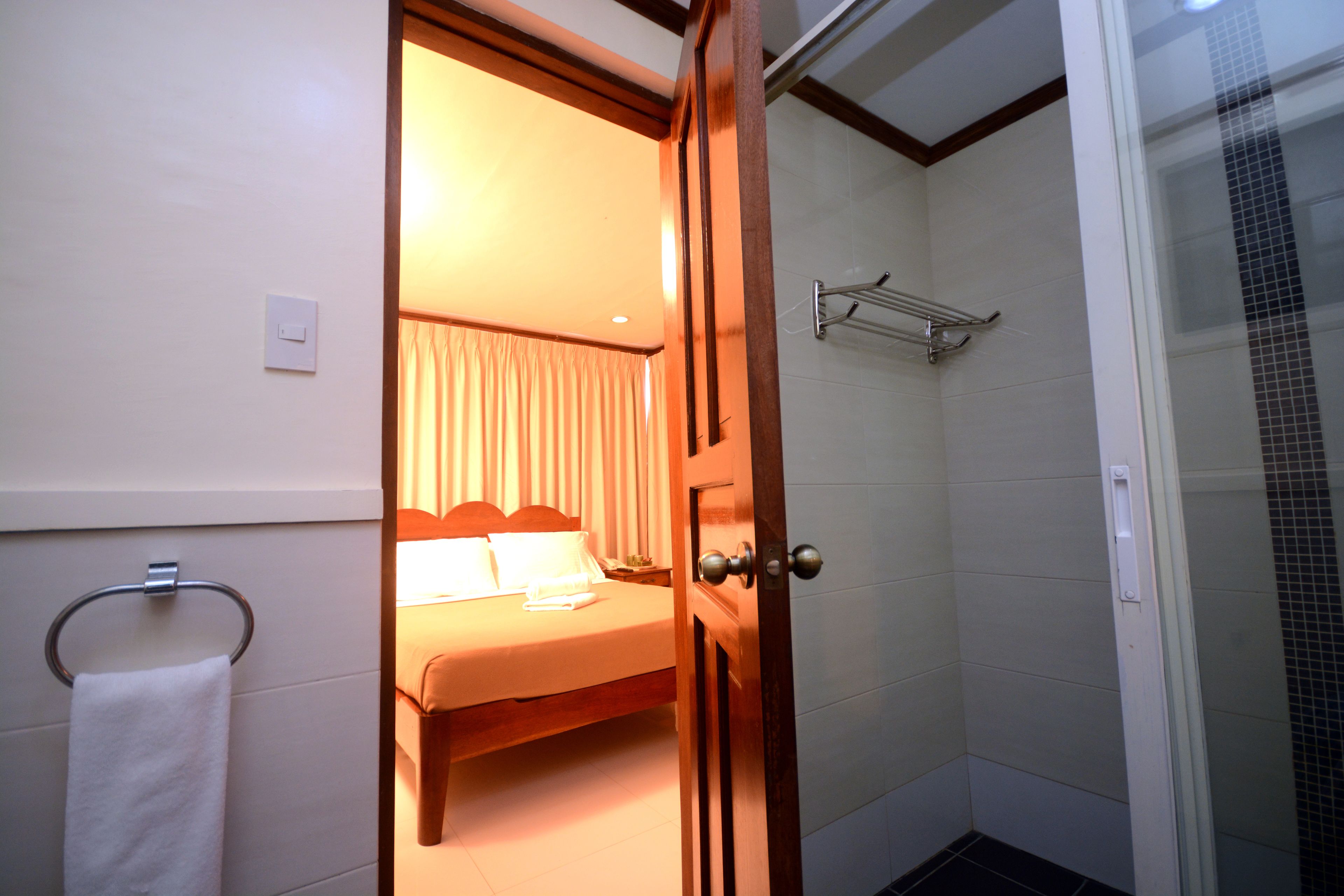 A hotel room with a bed, a shower area, and a towel rack.