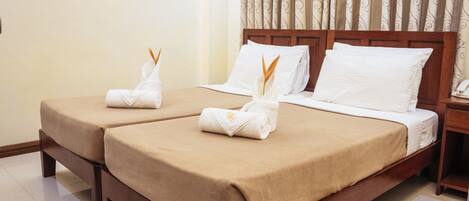 A hotel room with two beds, each with a beige bedspread and white pillows, and a wooden headboard.