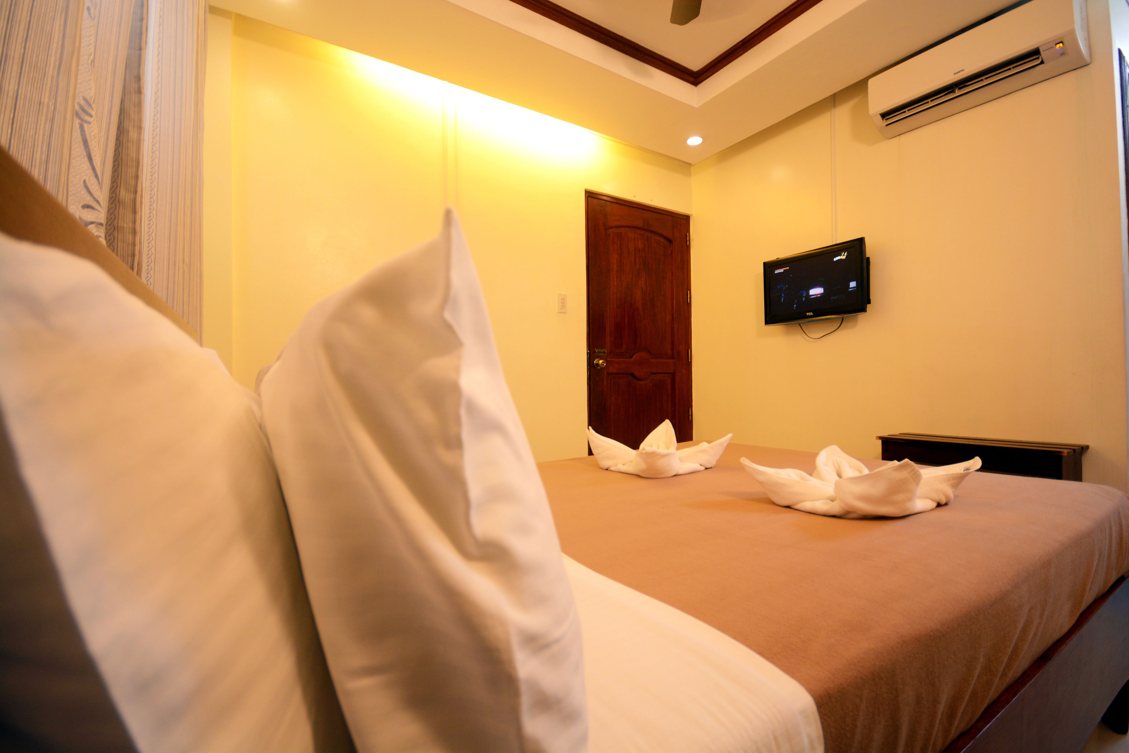Una habitación de hotel con una cama, almohadas, una puerta de madera y un televisor instalado en la pared.