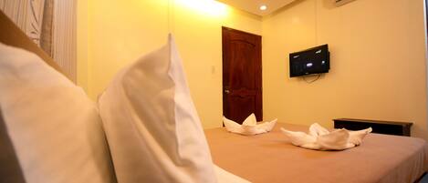 A hotel room with a bed, pillows, a wooden door, and a wall-mounted TV.